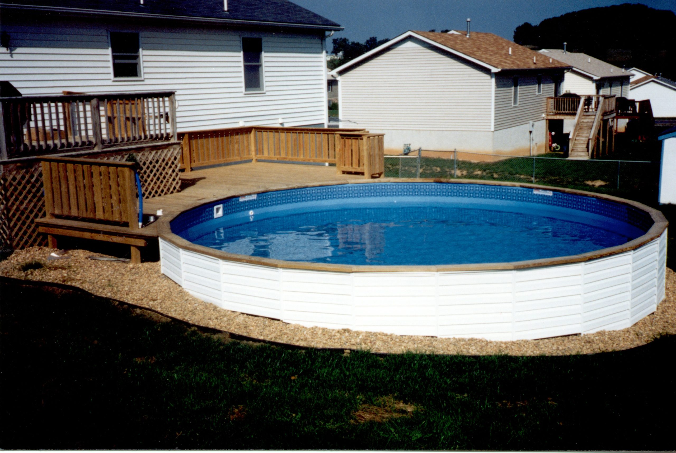Medallion St. Croix above ground swimming pool installed into a hillside with vinyl siding, wood top cap, and wood deck.
